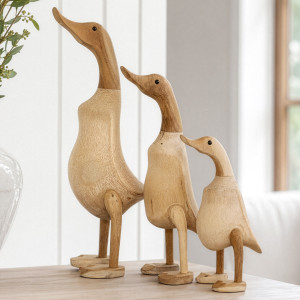 Three graduated natural wooden ducks displayed on a console beside a vase of foliage