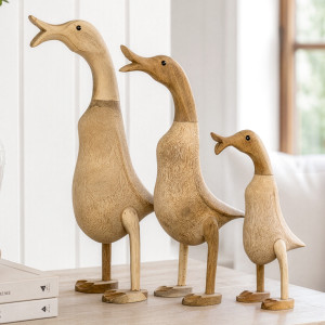 Close view of three natural wooden ducks with open beaks arranged on a light wood console
