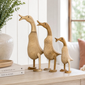 Three graduated natural wooden ducks with open beaks styled on a console beside books and a vase