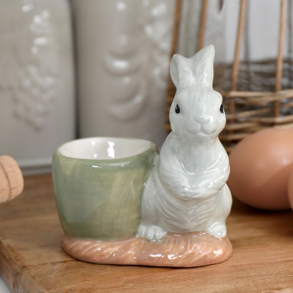 Handpainted grey bunny ceramic egg cup with pale green cup and blush base on a wooden board