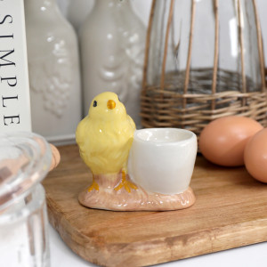 Yellow chick ceramic egg cup with a white cup and blush base styled on a wooden board