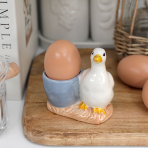 White duck ceramic egg cup with pale blue cup holding a brown egg on a wooden board