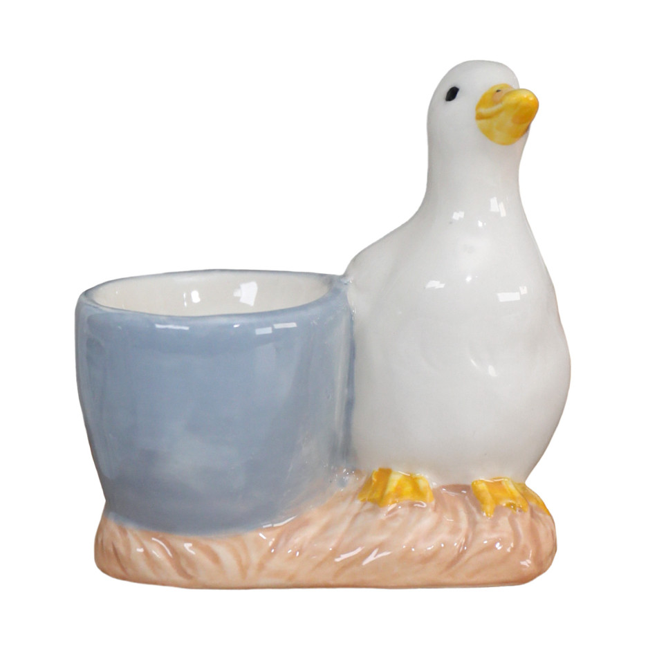 Handpainted white duck beside a pale blue ceramic egg cup on a blush textured base
