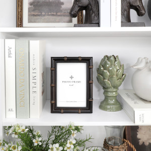 Black faux bamboo photo frame styled on a white shelf with books and green ceramic décor