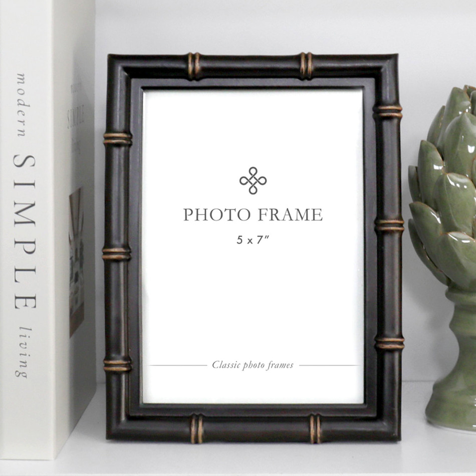 Rectangular black 5x7 photo frame with faux bamboo detailing and antique gold-toned accents on a shelf