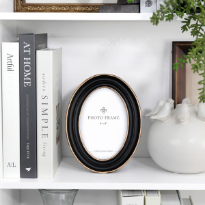 Vera oval black and gold photo frame styled on white shelving beside books and ceramic décor.