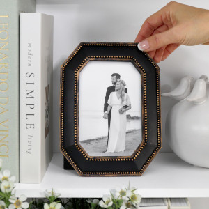 Black and gold beaded Ambrose photo frame holding a wedding photograph beside books and ceramic birds