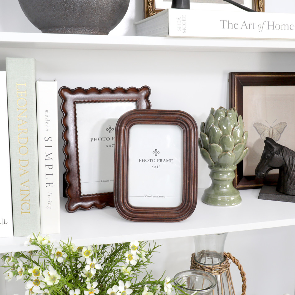 Orleans chestnut 4 x 6 photo frame styled on a white shelf with books, flowers and decorative objects.