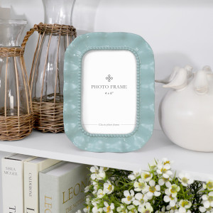 Aqua Sabina ruffle 4x6 photo frame styled on a white shelf with woven glass jugs and white ceramic décor.