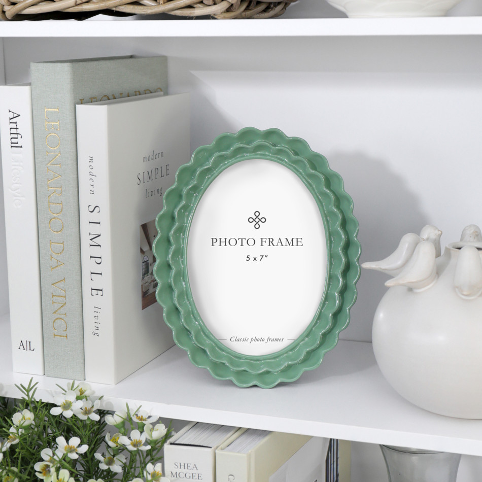 Lillian green scalloped oval 5x7 photo frame styled with books, white ceramic décor and flowers on a shelf.