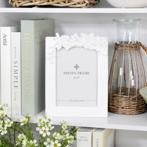 Dahlia floral white 5x7 photo frame styled with books, flowers and a wicker-wrapped glass vessel on a shelf.