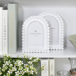 Snowdon beaded white 4x6 photo frame displayed with the coordinating larger frame, books and wicker-wrapped glass jugs on a white shelf.