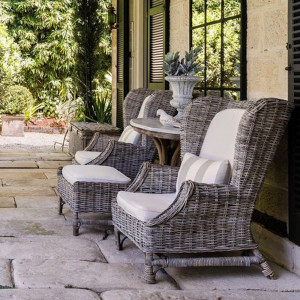 Rattan wingback armchair and footstool styled in a covered stone-paved outdoor setting