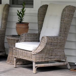 Grey-brown rattan wingback armchair with cream cushions beside a terracotta potted plant