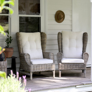 Pair of grey-brown rattan wingback armchairs with cream cushions viewed from the front
