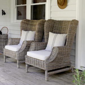 Two woven rattan wingback armchairs with cream cushions viewed at an angle on a verandah