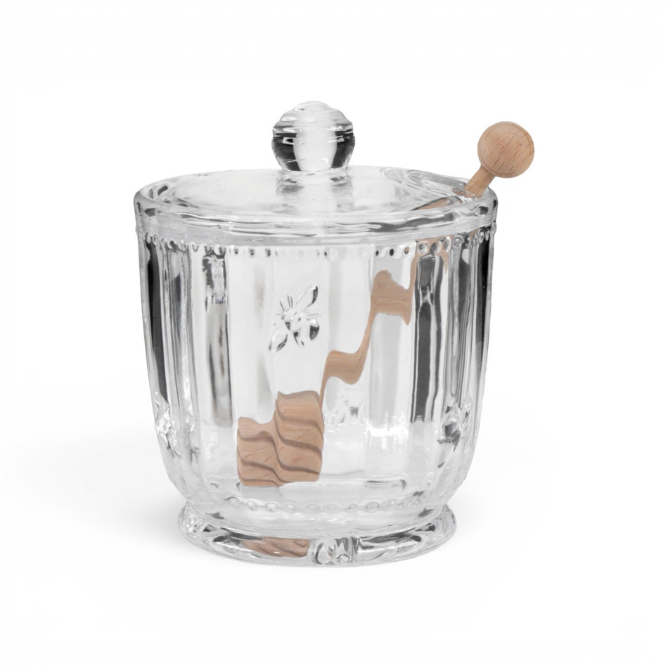 Glass honey jar with embossed bee motifs, wooden dipper and honey on a white background