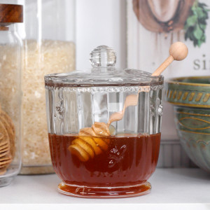 Glass honey jar filled with honey styled with pantry jars and a green mixing bowl