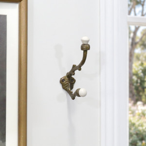 Antique gold double hook mounted on a white wall beside a framed print