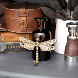 Wider view of the textured gold dragonfly wall hook styled on a dark console