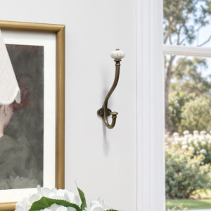 Tall antique gold double hook with white ceramic knob on a white wall