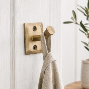 Gold iron nail wall hook holding a linen towel on white panelling beside leafy greenery