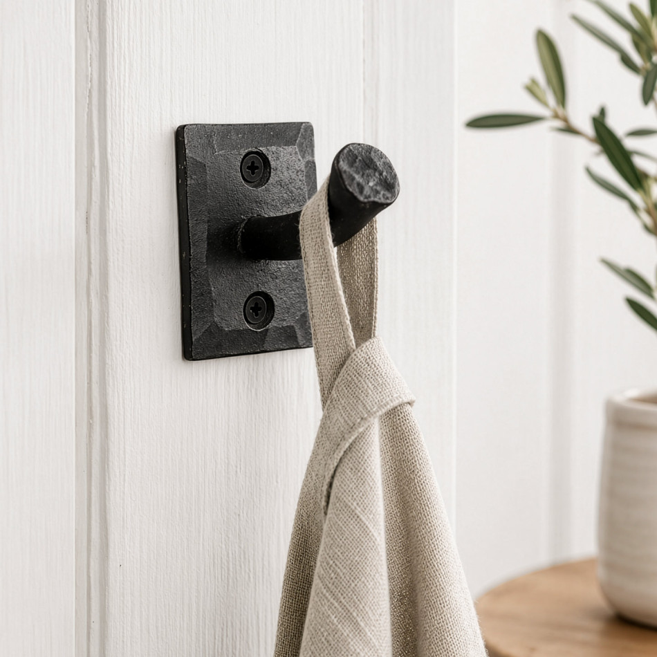 Black iron nail wall hook holding a linen towel on white panelling beside leafy greenery
