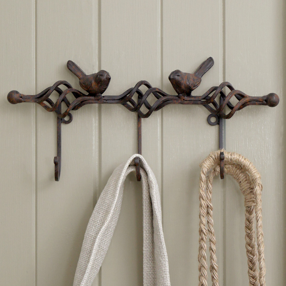 Rustic dark brown bird key hook rack mounted on sage panelling and holding natural fabric accessories