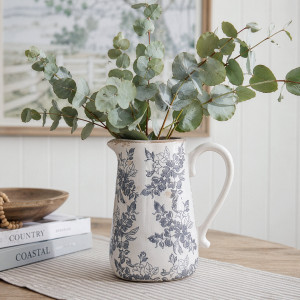 Norwood grey floral jug filled with eucalyptus beside stacked books and a wooden bowl