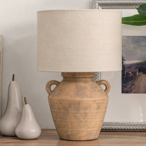 Rustic terracotta-effect table lamp with a beige linen shade beside ceramic pears and framed artwork