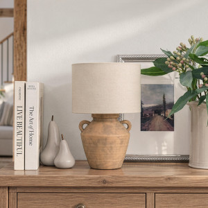 Terracotta-effect lamp on a timber console with books, ceramic pears, framed artwork and leafy stems