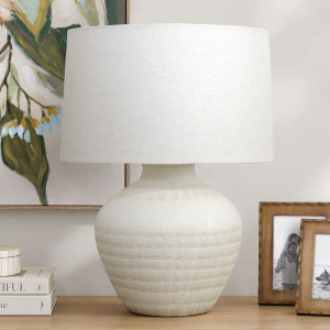 Fernando cream ceramic table lamp with linen shade, styled beside wooden photo frames and botanical artwork