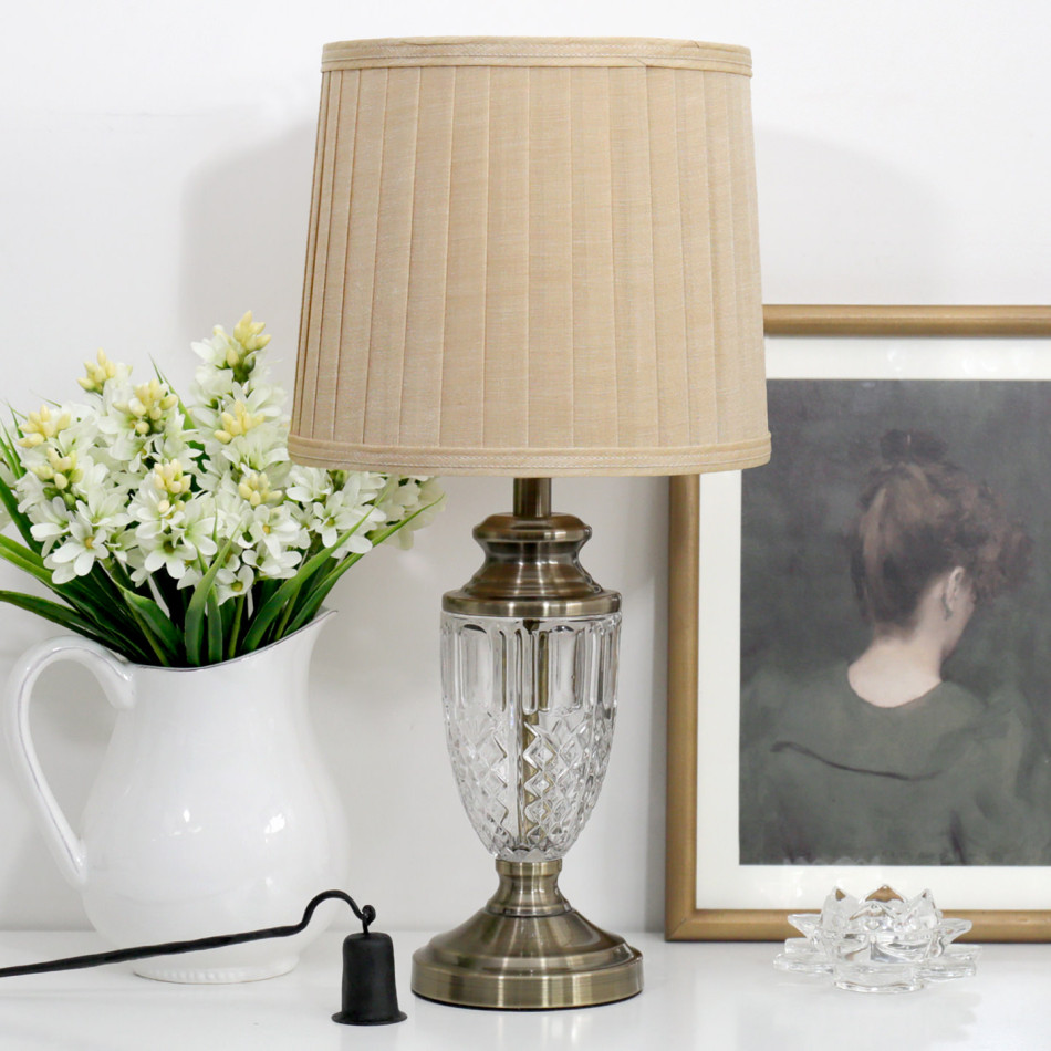 Molisana glass and antique gold table lamp with beige pleated shade beside white flowers and framed artwork