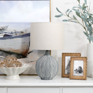 Sandringham blue lamp on a white console with boat artwork, wooden frames, fishing floats and leafy stems