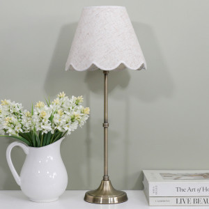 Claudia antique gold table lamp with scalloped linen shade, styled beside white flowers and stacked books