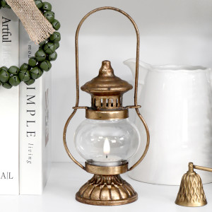 Yuletide aged gold tealight lantern with a lit tealight, styled beside books and a white ceramic jug.