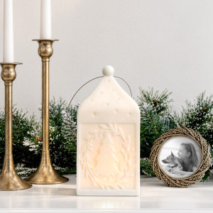 Illuminated Large Silent Night lantern styled beside gold candlesticks, a round photo frame and frosted pine greenery.