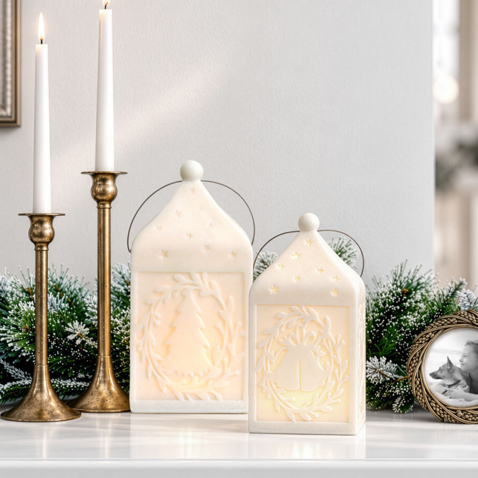 Large tree-design Silent Night lantern beside the smaller bell-design lantern, both illuminated among frosted greenery and gold candlesticks.