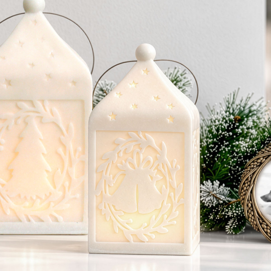 Illuminated Small Silent Night lantern with bell and leafy wreath detailing, beside the larger tree-design lantern and frosted greenery.