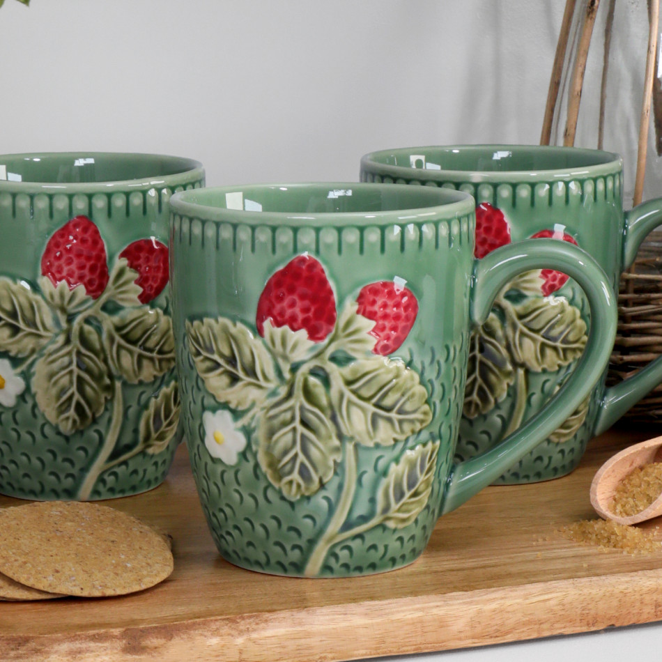 Three green strawberry ceramic mugs styled together on a wooden board