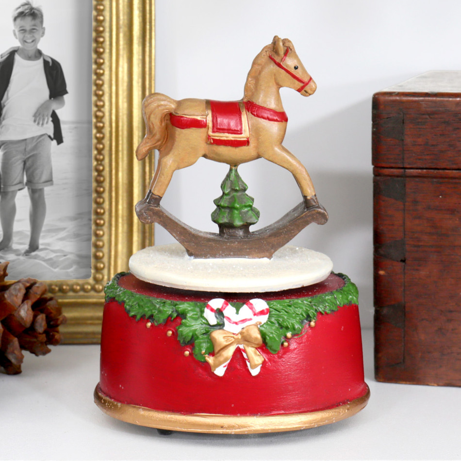 Close-up of Merry & Bright music box with a rocking horse above a red base decorated with greenery and candy canes