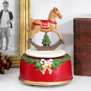 Close-up of Merry & Bright music box with a rocking horse above a red base decorated with greenery and candy canes