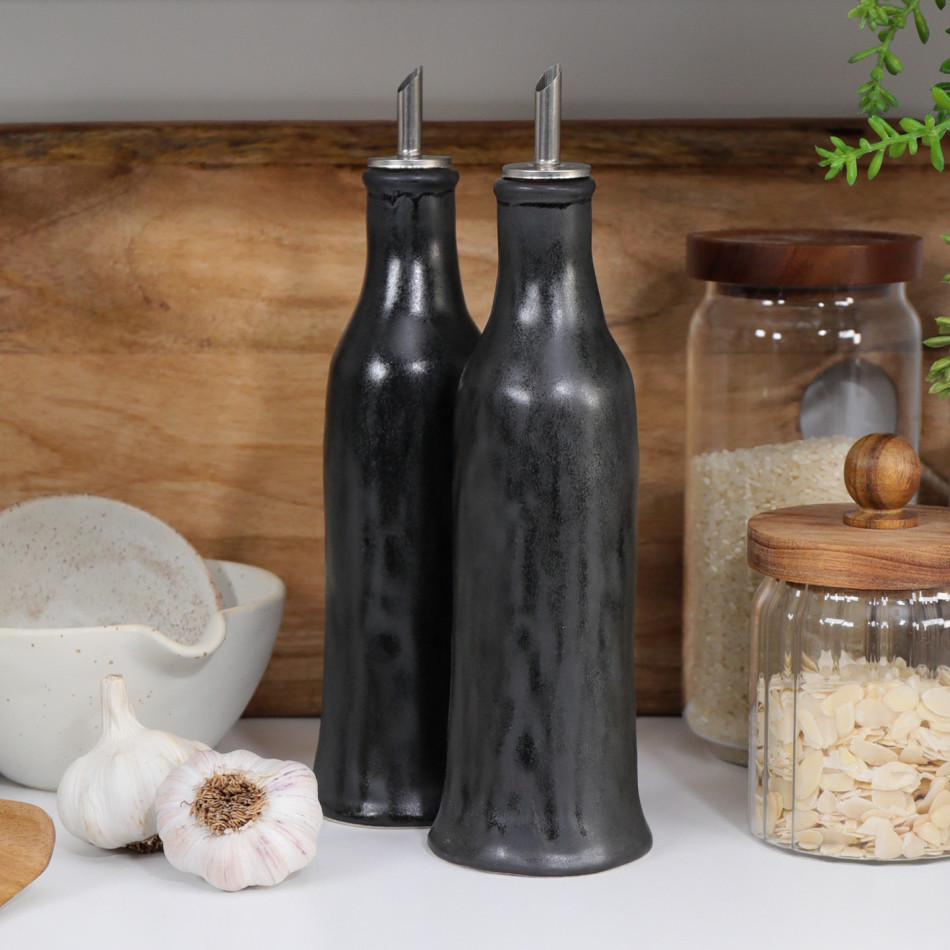 Set of two black reactive-glaze ceramic oil and vinegar bottles styled on a kitchen bench.