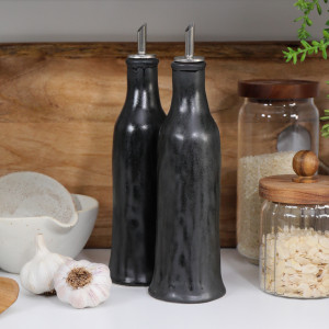 Set of two black reactive-glaze ceramic oil and vinegar bottles styled on a kitchen bench.
