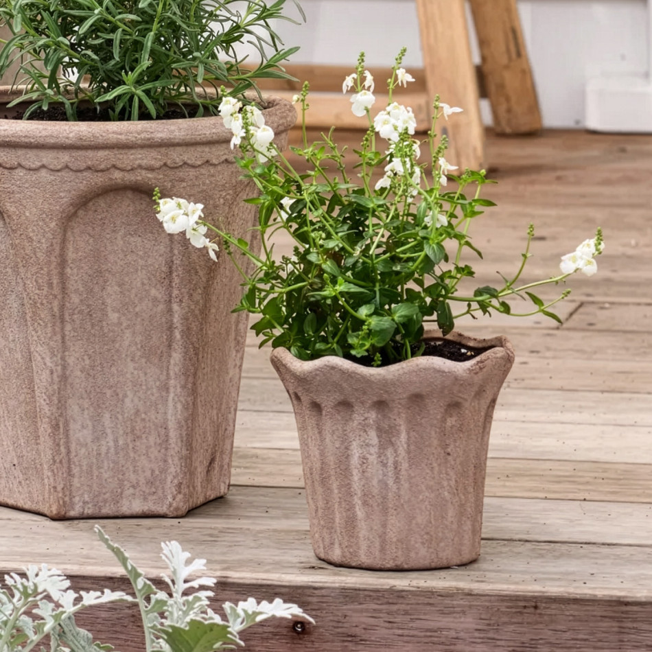 Small fluted sand terracotta plant pot with white flowers beside a coordinating arched planter