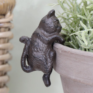 Close-up of a dark brown cast iron kitten pot hanger with curved paws and a curled tail on a pale pot rim