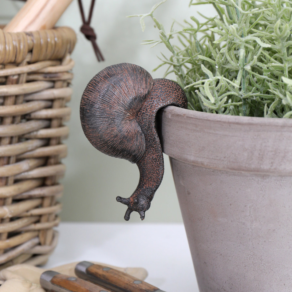 Vintage brown resin snail hanging from a plant pot beside a woven basket, gardening gloves and secateurs