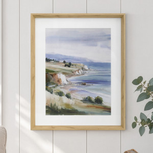 White Cliffs coastal print with blue sea, grassy slopes and a natural-toned wood-effect frame on a white panelled wall
