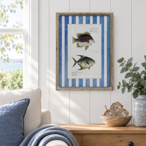 Framed print of two banded fish above a timber cabinet beside a cream armchair and eucalyptus