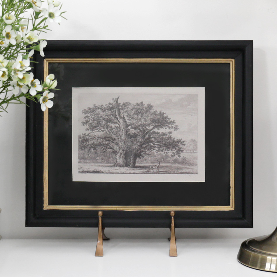 Sandhurst vintage tree print in a black and gold frame displayed beside white flowers and a brass lamp.